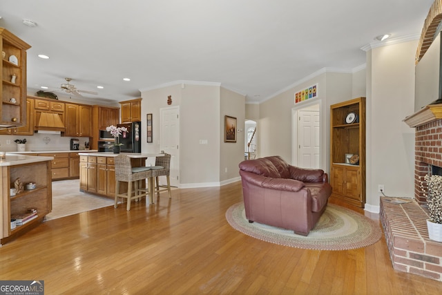 living area featuring baseboards, light wood-style flooring, ornamental molding, a brick fireplace, and recessed lighting