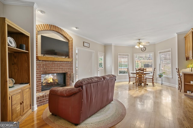 living room featuring light wood-style floors, a brick fireplace, baseboards, and crown molding