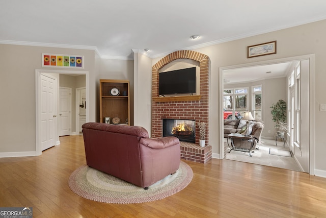 living area featuring a brick fireplace, crown molding, light wood-style flooring, and baseboards