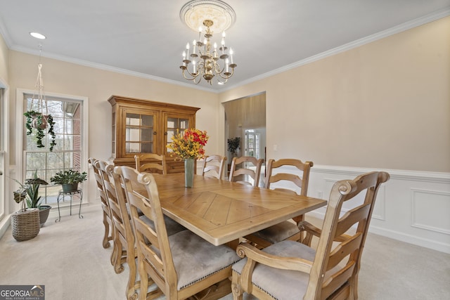 dining area with light colored carpet, a wainscoted wall, crown molding, a decorative wall, and a notable chandelier