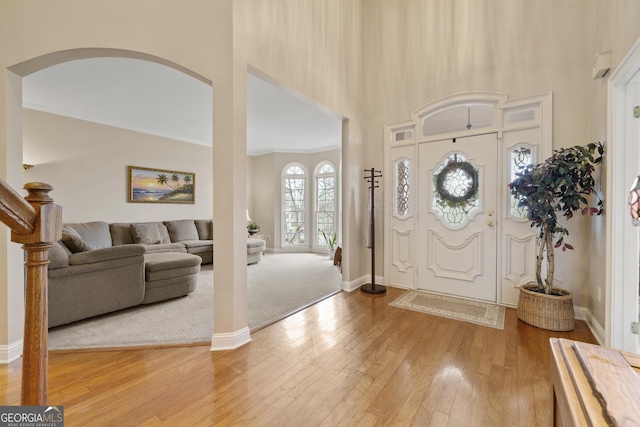 foyer entrance with a towering ceiling, light wood-style flooring, ornamental molding, and baseboards