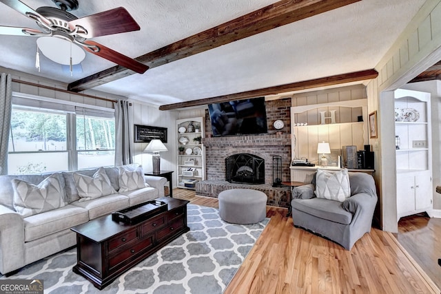 living area with beam ceiling, a fireplace, a textured ceiling, and wood finished floors