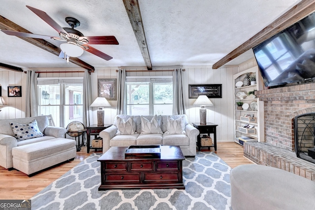 living room featuring a textured ceiling, wooden walls, wood finished floors, a brick fireplace, and beamed ceiling