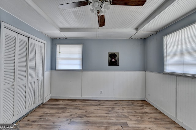 unfurnished bedroom featuring a wainscoted wall, ceiling fan, a closet, and wood finished floors