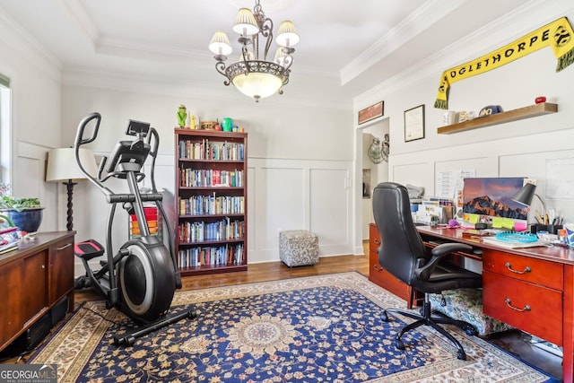 office space featuring a tray ceiling, a decorative wall, wood finished floors, and ornamental molding