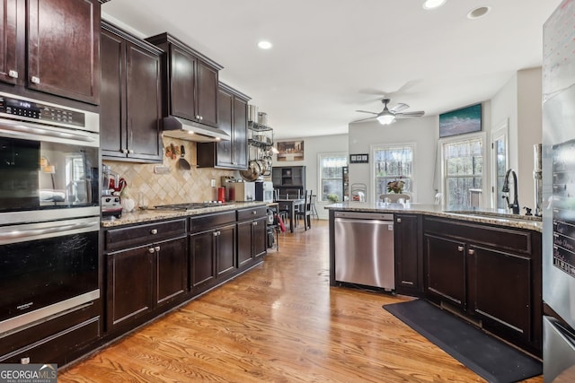 kitchen featuring light wood-style flooring, stainless steel appliances, a sink, backsplash, and light stone countertops