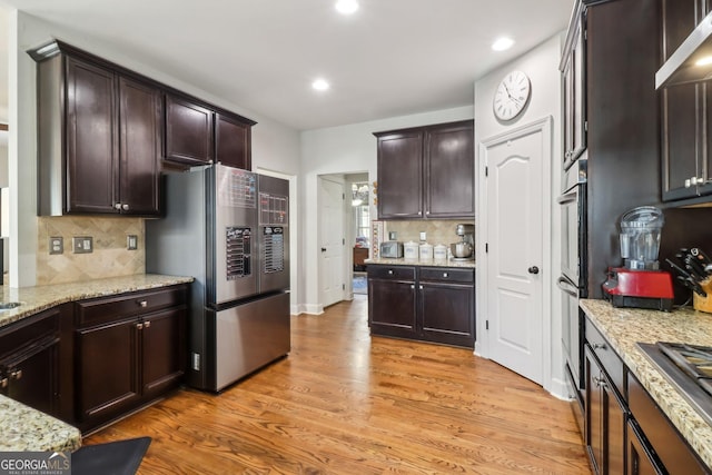 kitchen featuring dark brown cabinetry, tasteful backsplash, appliances with stainless steel finishes, light stone countertops, and light wood-type flooring