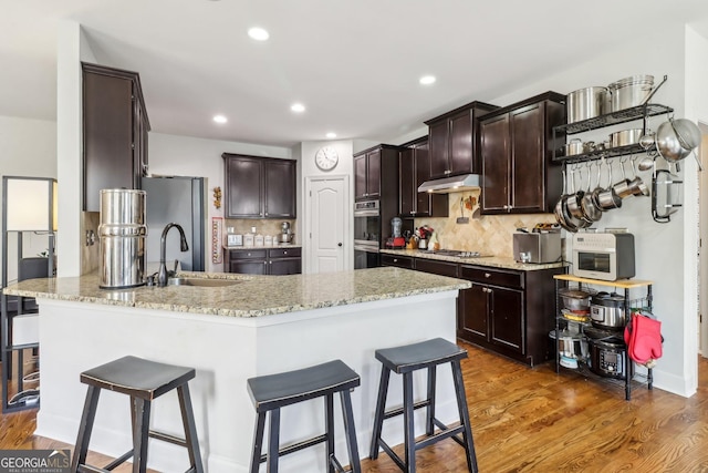 kitchen with under cabinet range hood, a peninsula, stainless steel appliances, wood finished floors, and a sink