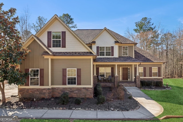 craftsman-style house with a shingled roof, stone siding, covered porch, a front lawn, and board and batten siding