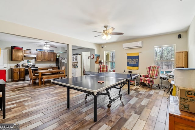 game room with ceiling fan, an AC wall unit, and light wood-style floors