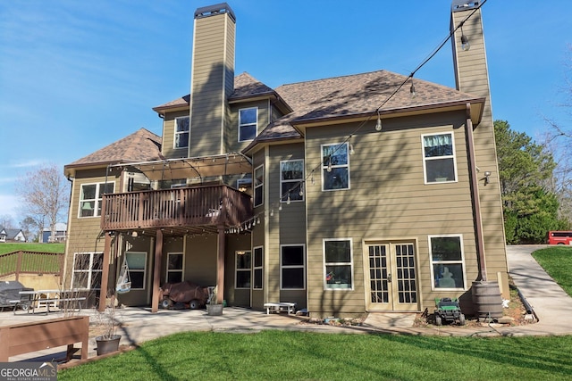 back of property featuring a lawn, french doors, a chimney, a wooden deck, and a patio area