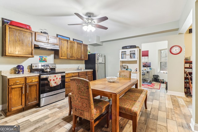 kitchen featuring light countertops, light wood-style flooring, appliances with stainless steel finishes, a sink, and under cabinet range hood