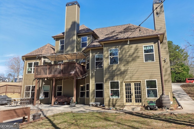 rear view of property with a wooden deck, french doors, a patio, a chimney, and a yard