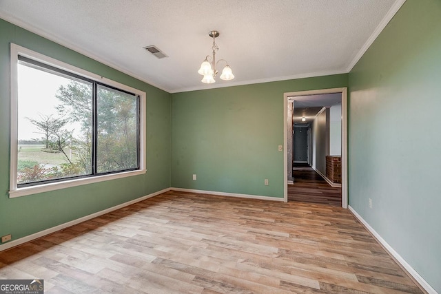 spare room featuring visible vents, light wood-style floors, baseboards, ornamental molding, and an inviting chandelier