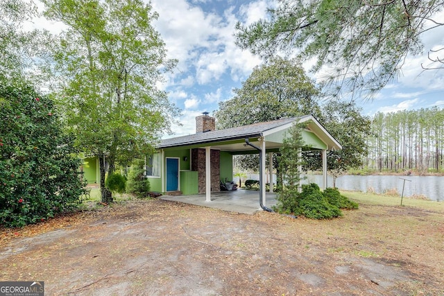 exterior space with driveway, a carport, a chimney, and a water view