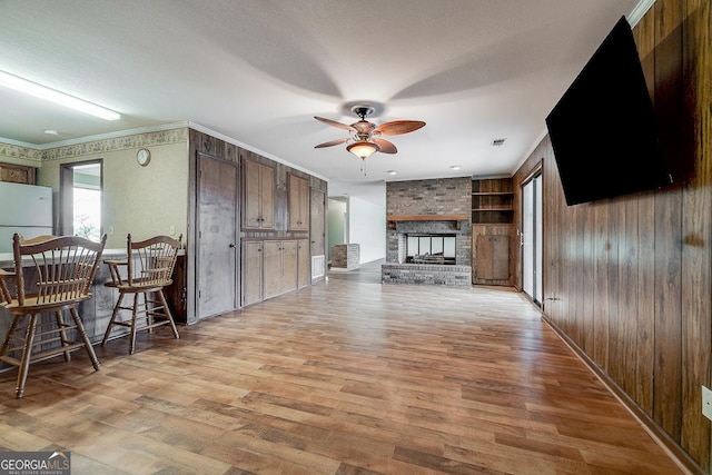 living area with visible vents, a ceiling fan, ornamental molding, a brick fireplace, and light wood-type flooring