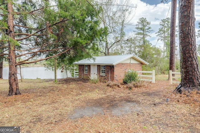 view of front facade featuring a water view, fence, metal roof, and brick siding