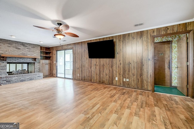 unfurnished living room featuring a brick fireplace, crown molding, visible vents, and wood finished floors