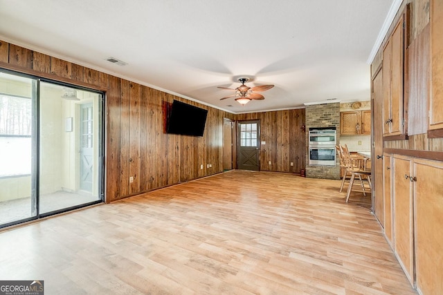 unfurnished living room with light wood finished floors, wood walls, a ceiling fan, and crown molding