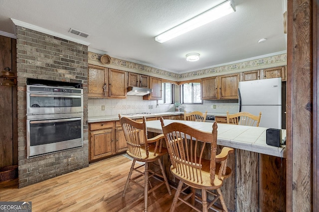 kitchen featuring white appliances, visible vents, a breakfast bar, light wood-type flooring, and under cabinet range hood