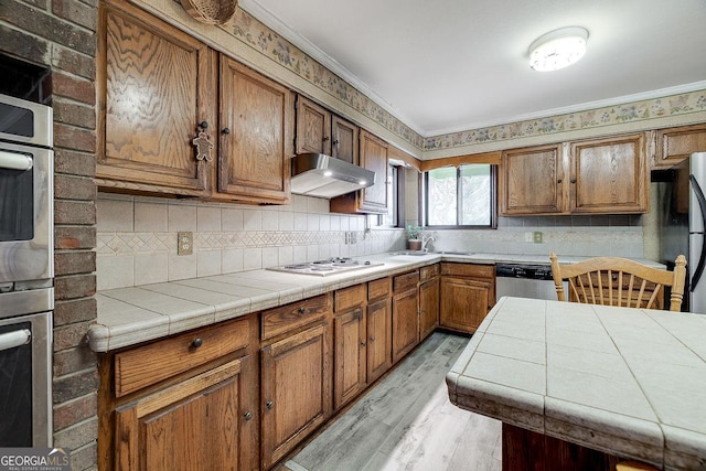 kitchen featuring stainless steel appliances, ventilation hood, light wood-type flooring, tasteful backsplash, and brown cabinetry