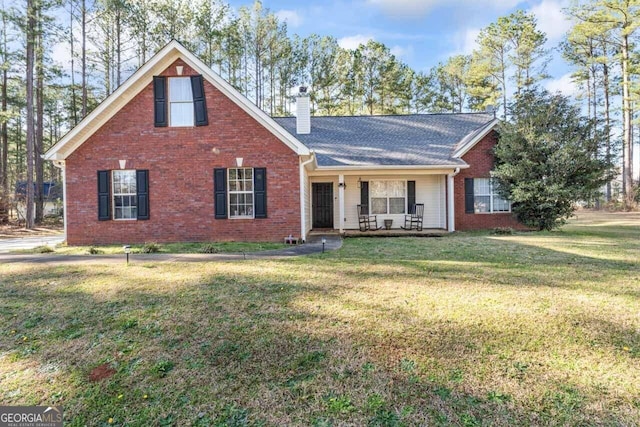 traditional-style house featuring brick siding, a chimney, a porch, and a front yard