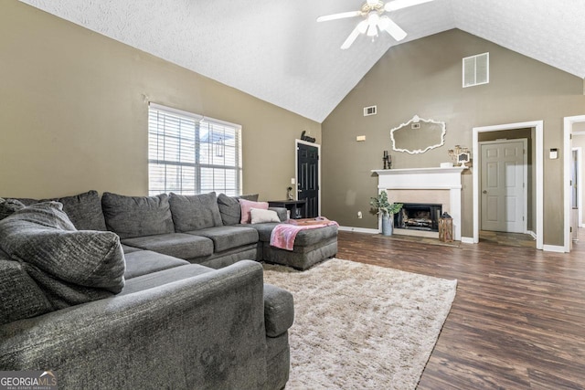 living room featuring high vaulted ceiling, dark wood-type flooring, a fireplace with flush hearth, a ceiling fan, and visible vents