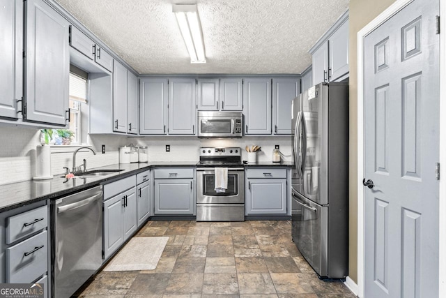 kitchen with a sink, gray cabinets, dark countertops, and stainless steel appliances