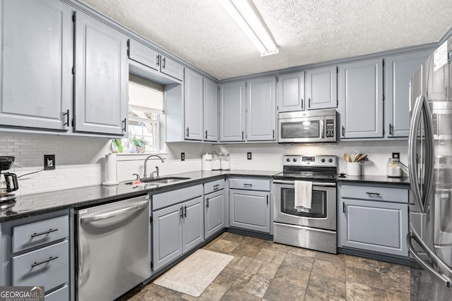 kitchen featuring a sink, appliances with stainless steel finishes, stone finish floor, gray cabinetry, and backsplash