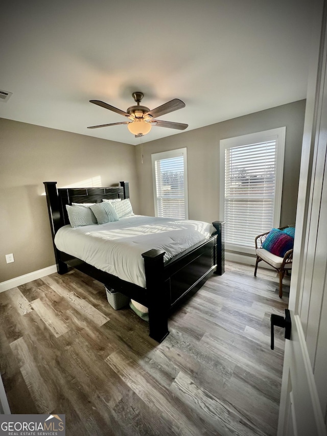 bedroom featuring ceiling fan, visible vents, baseboards, and wood finished floors