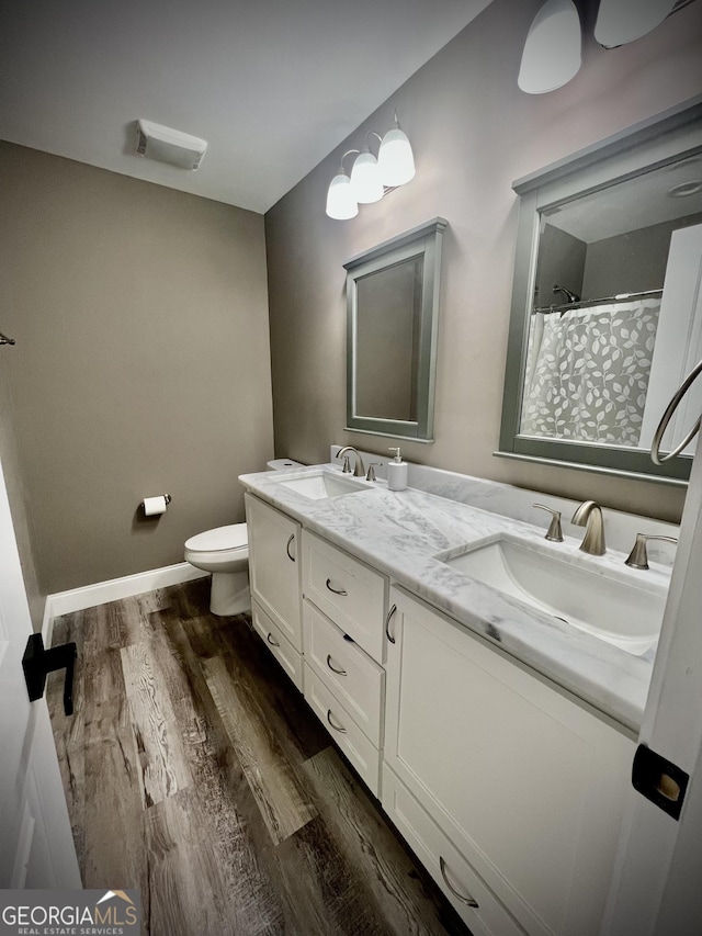 full bathroom featuring double vanity, wood finished floors, a sink, and toilet