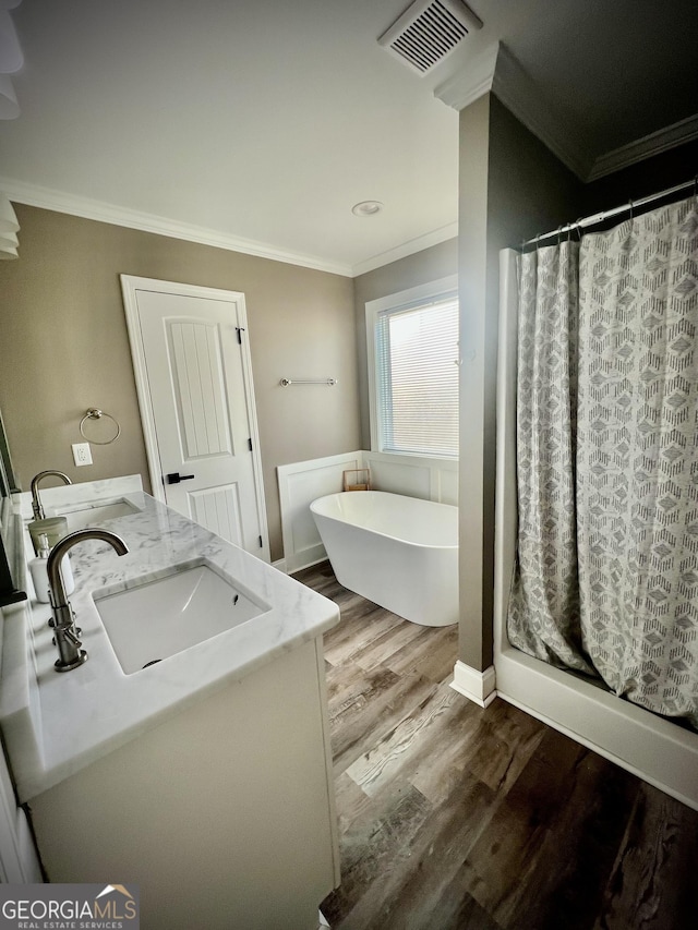 full bath with visible vents, a soaking tub, wood finished floors, crown molding, and a sink