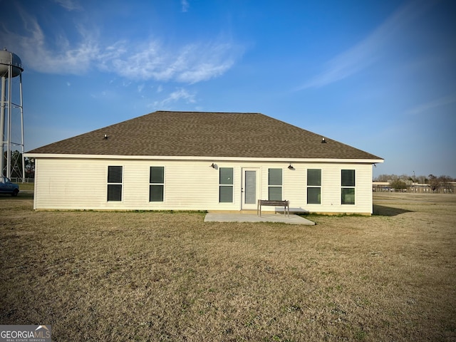 rear view of property featuring a patio area, a shingled roof, and a lawn