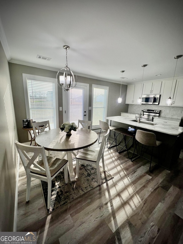 dining space with a healthy amount of sunlight, dark wood-style floors, visible vents, and ornamental molding