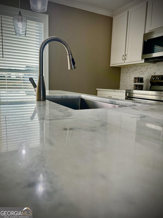 room details featuring white cabinets, decorative backsplash, appliances with stainless steel finishes, light stone countertops, and crown molding