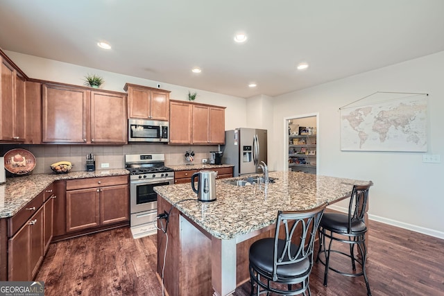 kitchen with stainless steel appliances, a sink, dark wood finished floors, a kitchen bar, and a center island with sink