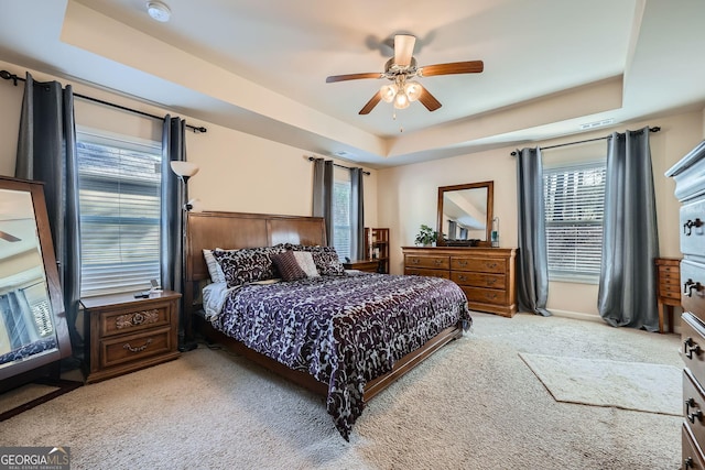 carpeted bedroom with a tray ceiling and a ceiling fan