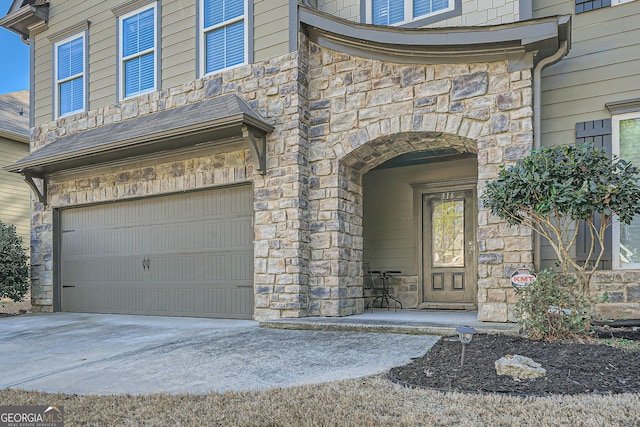 view of exterior entry with a garage, stone siding, and concrete driveway