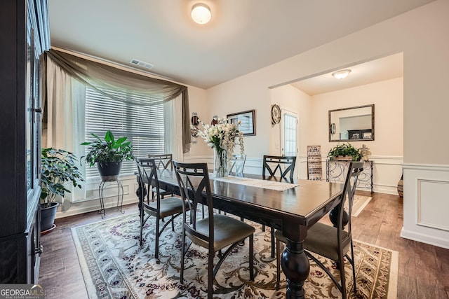 dining area featuring visible vents, a wainscoted wall, dark wood finished floors, and a decorative wall