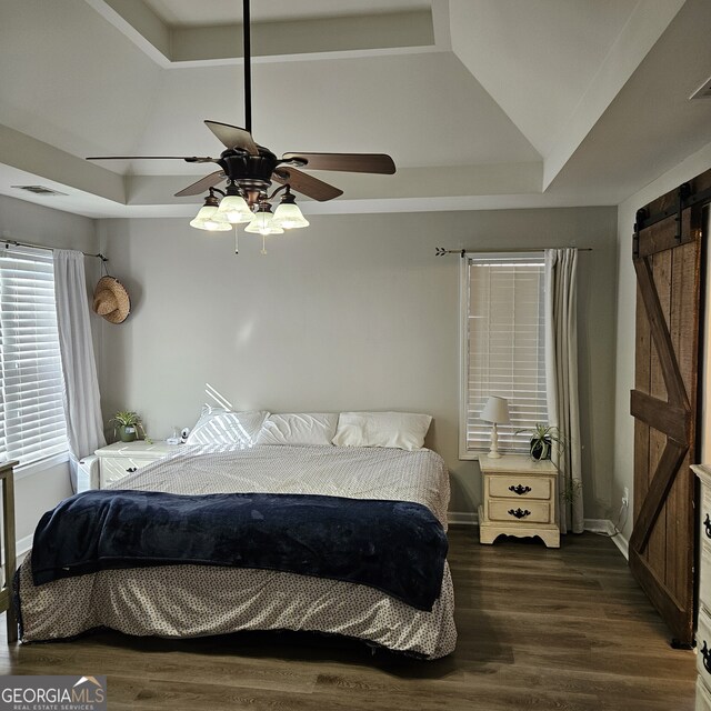 bedroom featuring wood finished floors, a raised ceiling, visible vents, and a barn door