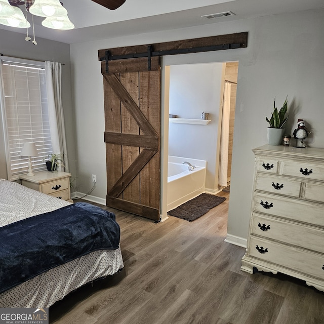 bedroom with a barn door, baseboards, visible vents, a ceiling fan, and wood finished floors