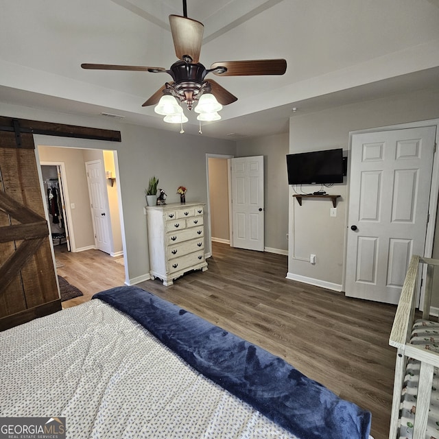 bedroom with a ceiling fan, a barn door, baseboards, and wood finished floors