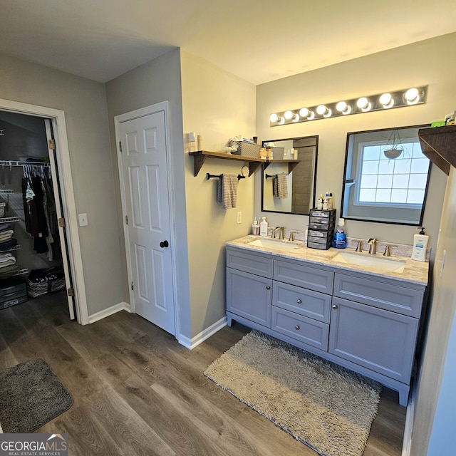 bathroom with double vanity, wood finished floors, a sink, and baseboards