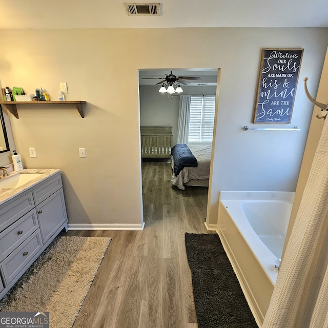 ensuite bathroom featuring visible vents, connected bathroom, wood finished floors, baseboards, and a bath