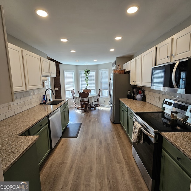 kitchen featuring wood finished floors, appliances with stainless steel finishes, a sink, and green cabinetry