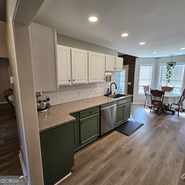 kitchen featuring decorative backsplash, green cabinetry, wood finished floors, stainless steel dishwasher, and a sink