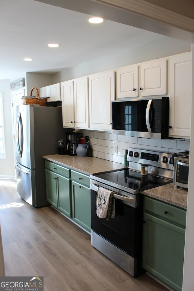 kitchen featuring light wood finished floors, white cabinets, decorative backsplash, stainless steel appliances, and green cabinetry