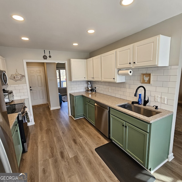 kitchen with wood finished floors, stainless steel appliances, white cabinetry, green cabinets, and a sink