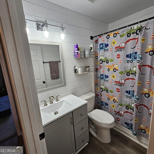 bathroom with a shower with shower curtain, toilet, wooden walls, vanity, and wood finished floors