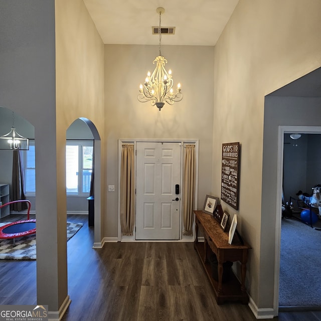 entrance foyer featuring visible vents, arched walkways, dark wood-style floors, an inviting chandelier, and a high ceiling